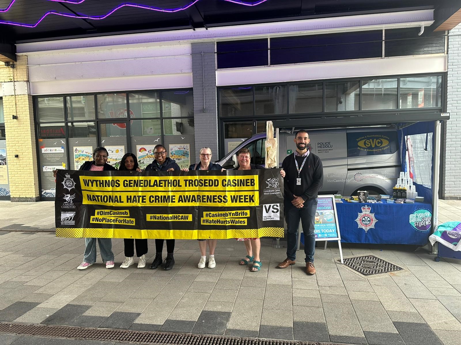 Pobl yn sefyll gyda poster troseddau casineb